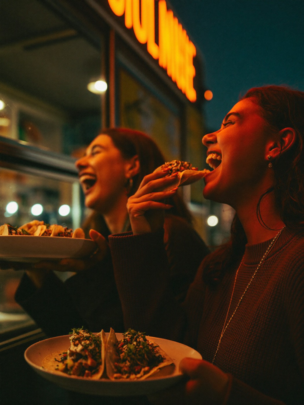 Friends laughing over street food at a neon-lit food truck window