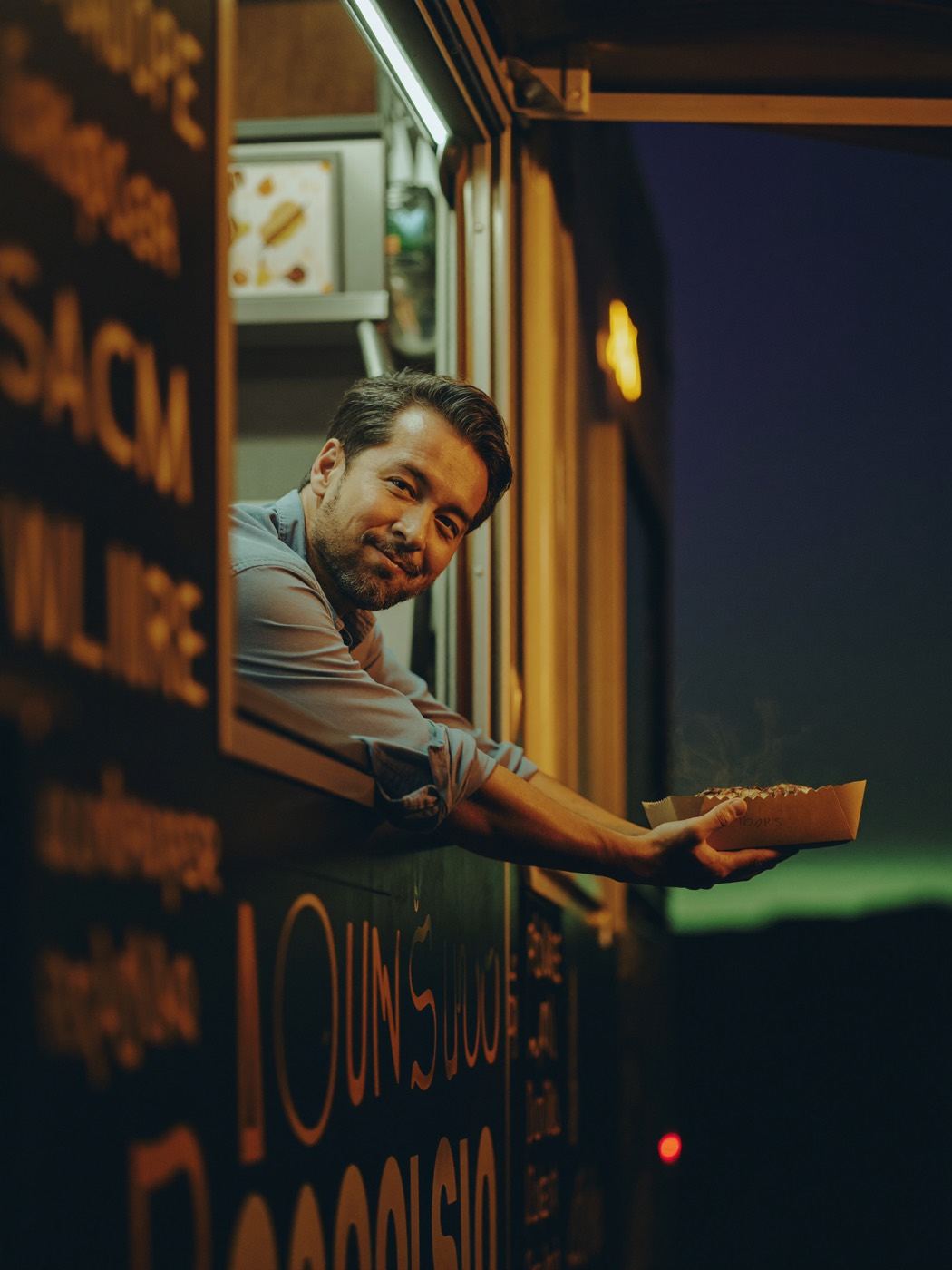 A food truck owner handing an order out the window at night